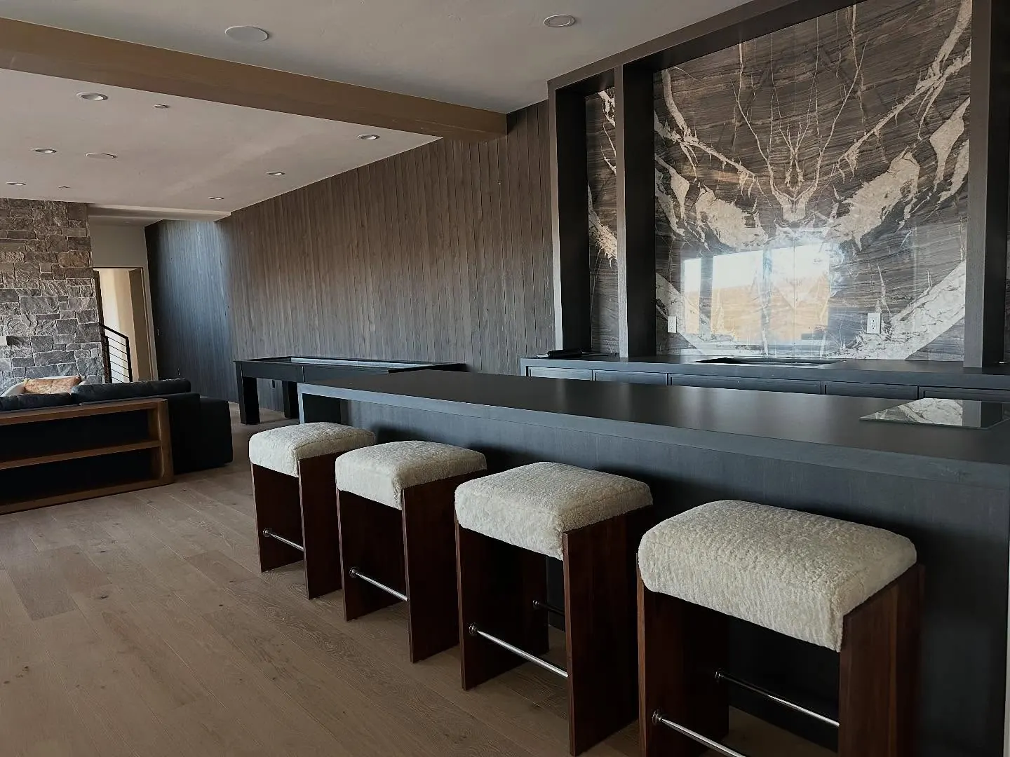 Four walnut barstools with cream shearling seats at a dark bar.