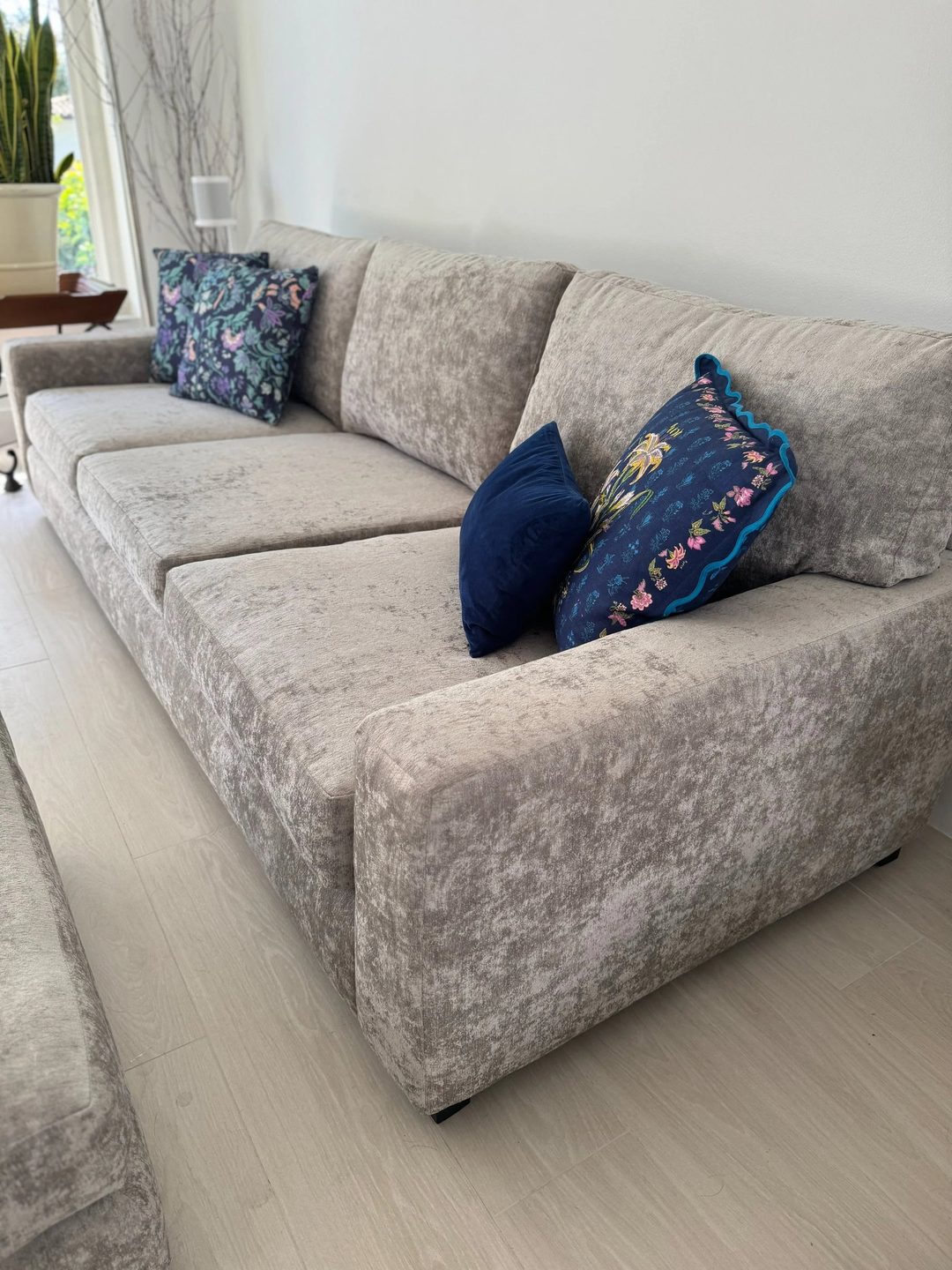A deep three-seat sofa in silver-grey crushed velvet, with navy velvet and embroidered floral pillows.