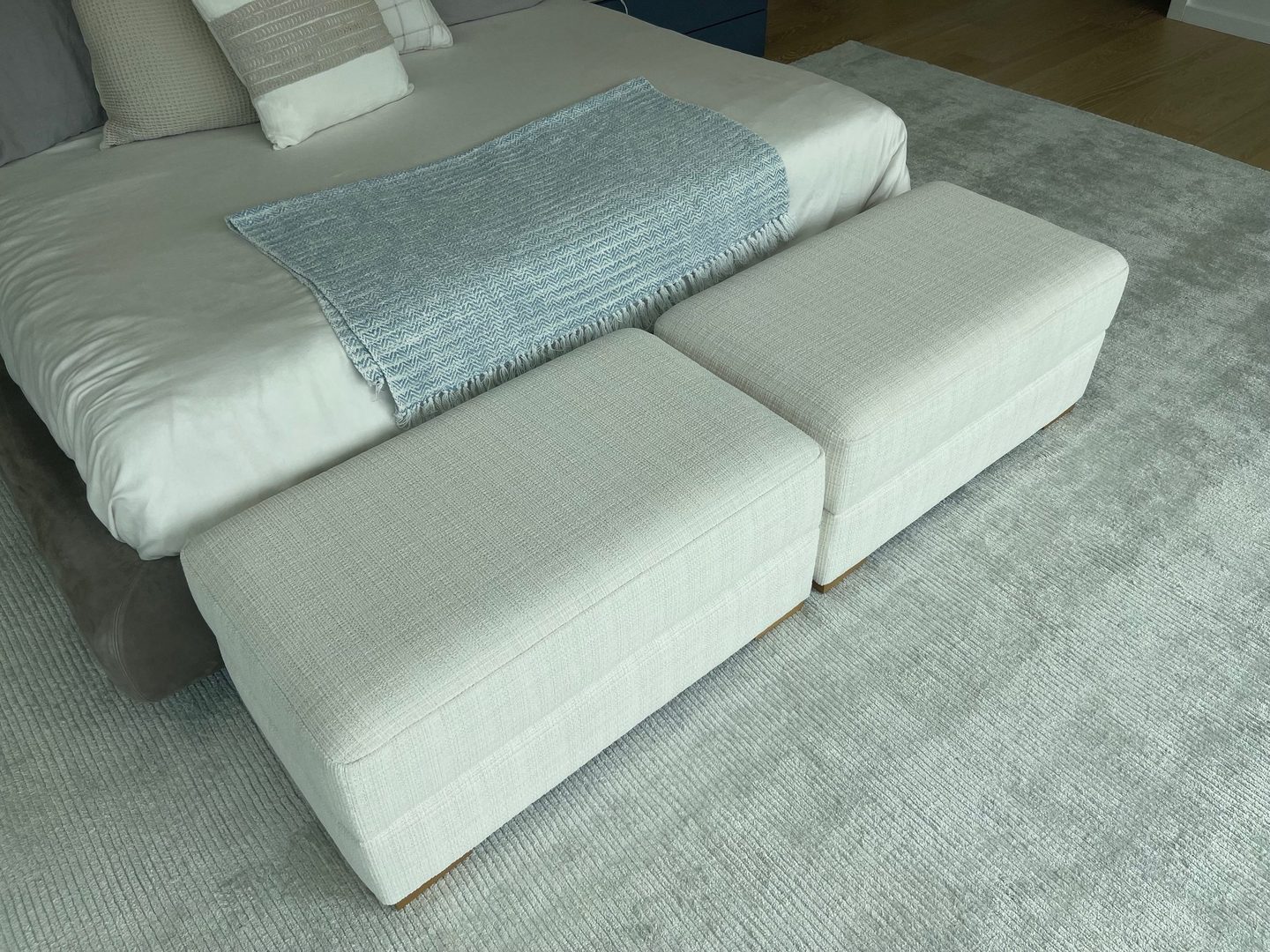 Two cream upholstered benches side by side at the foot of a bed, on a pale grey rug.