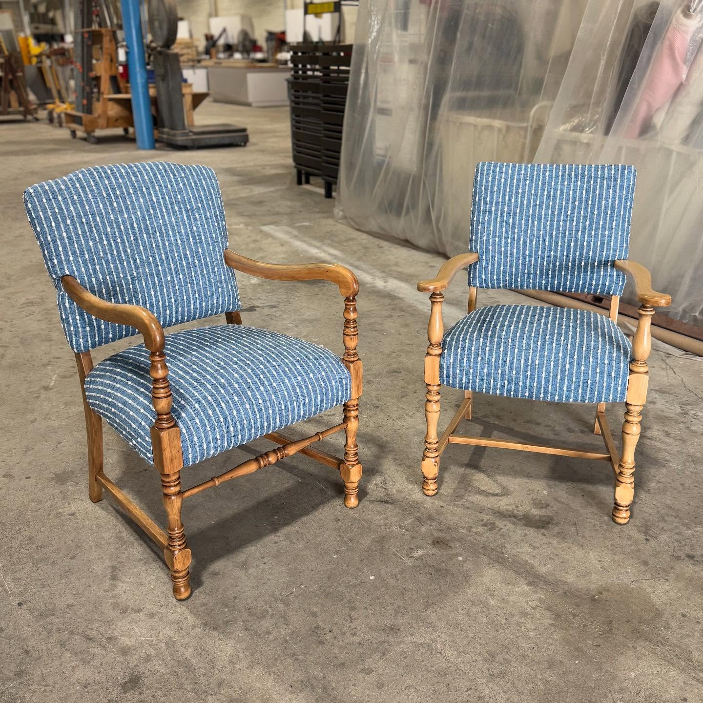 Two wooden armchairs newly covered in blue fabric with thin white stripes, standing in the workshop.