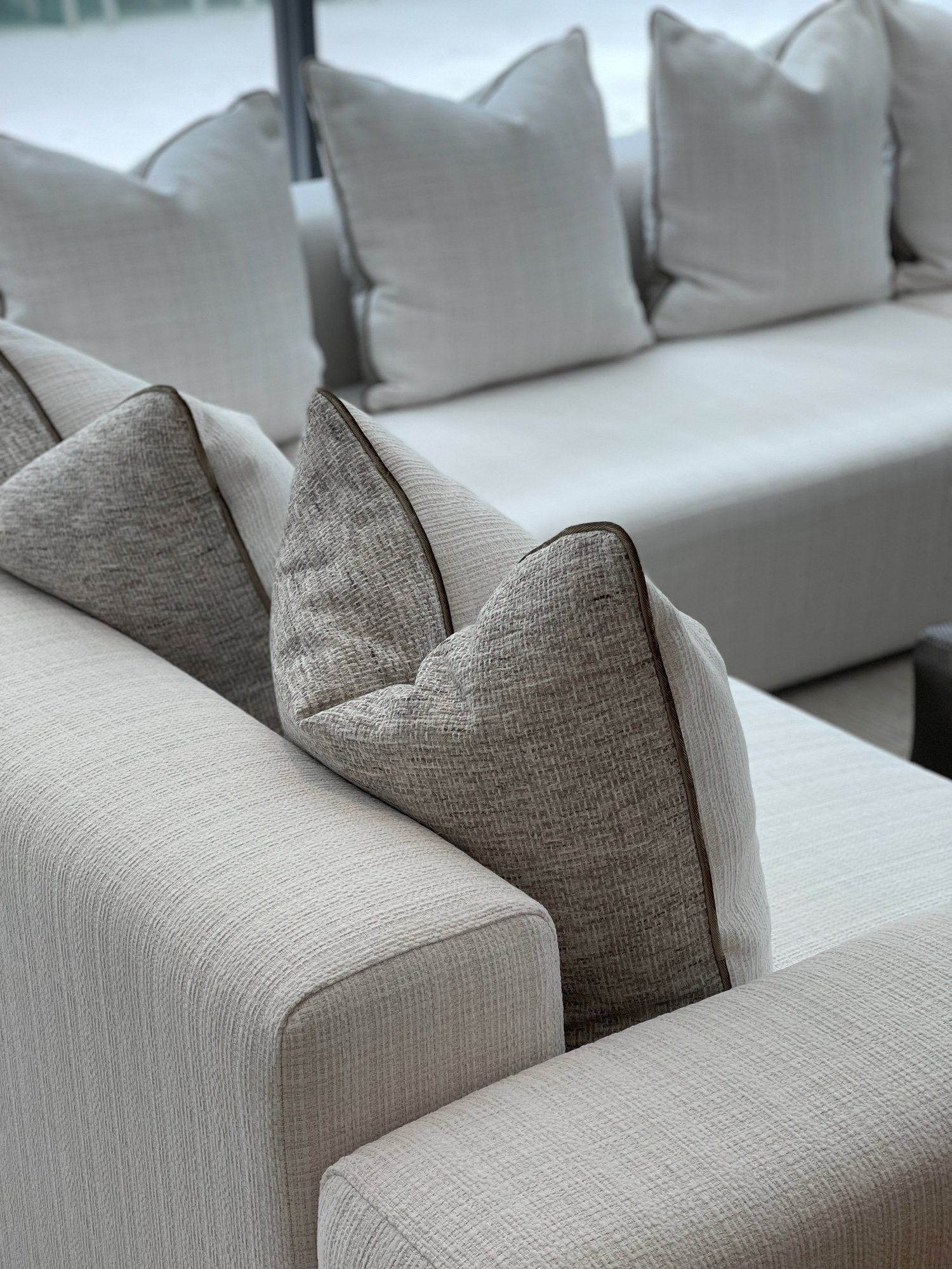 Close-up of a textured white sofa arm with grey tweed pillows piped in brown, and more white pillows along the sectional behind.