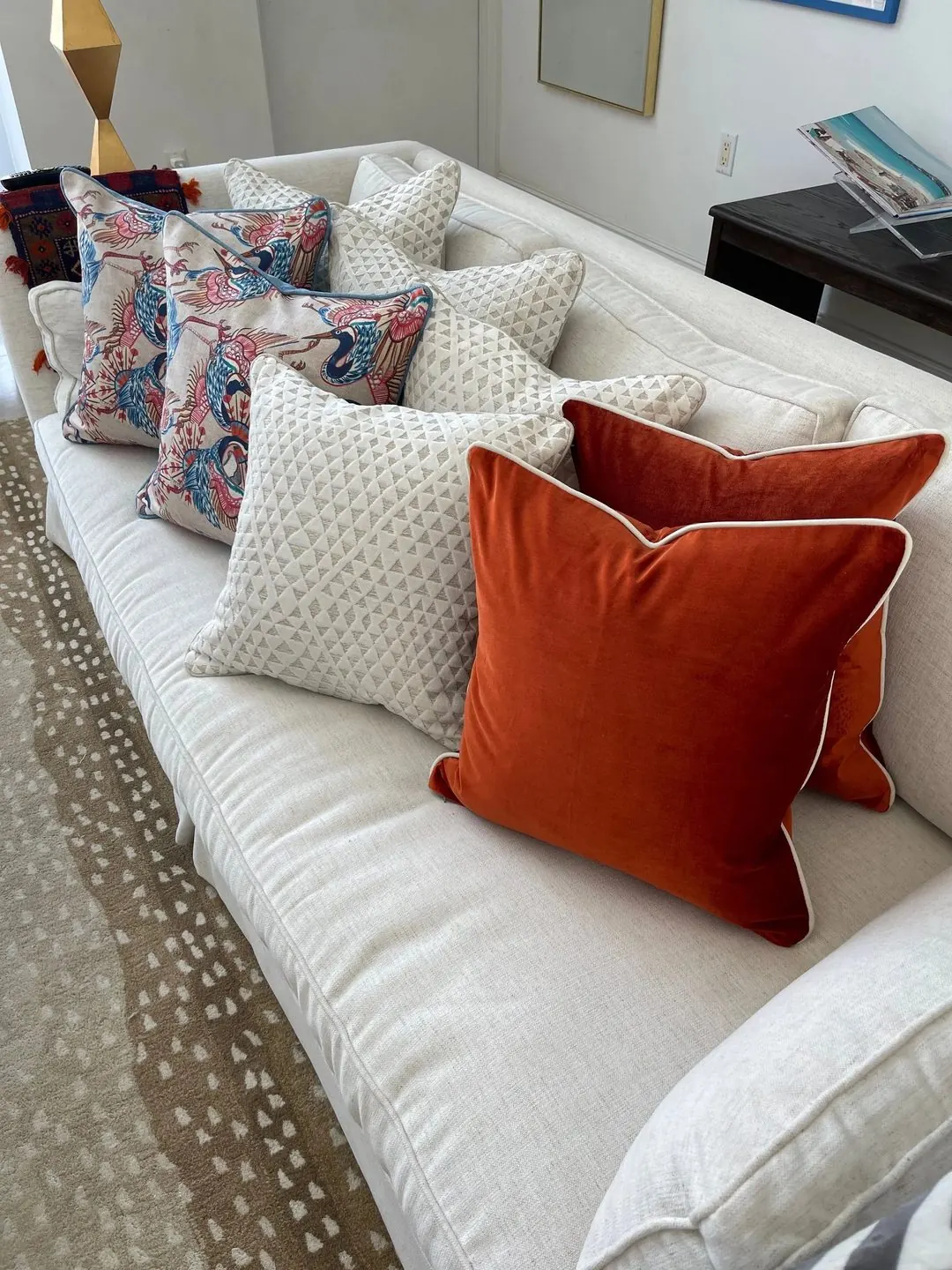 A cream sofa layered with rust velvet pillows, cream diamond-weave pillows, and pillows printed with colourful birds.
