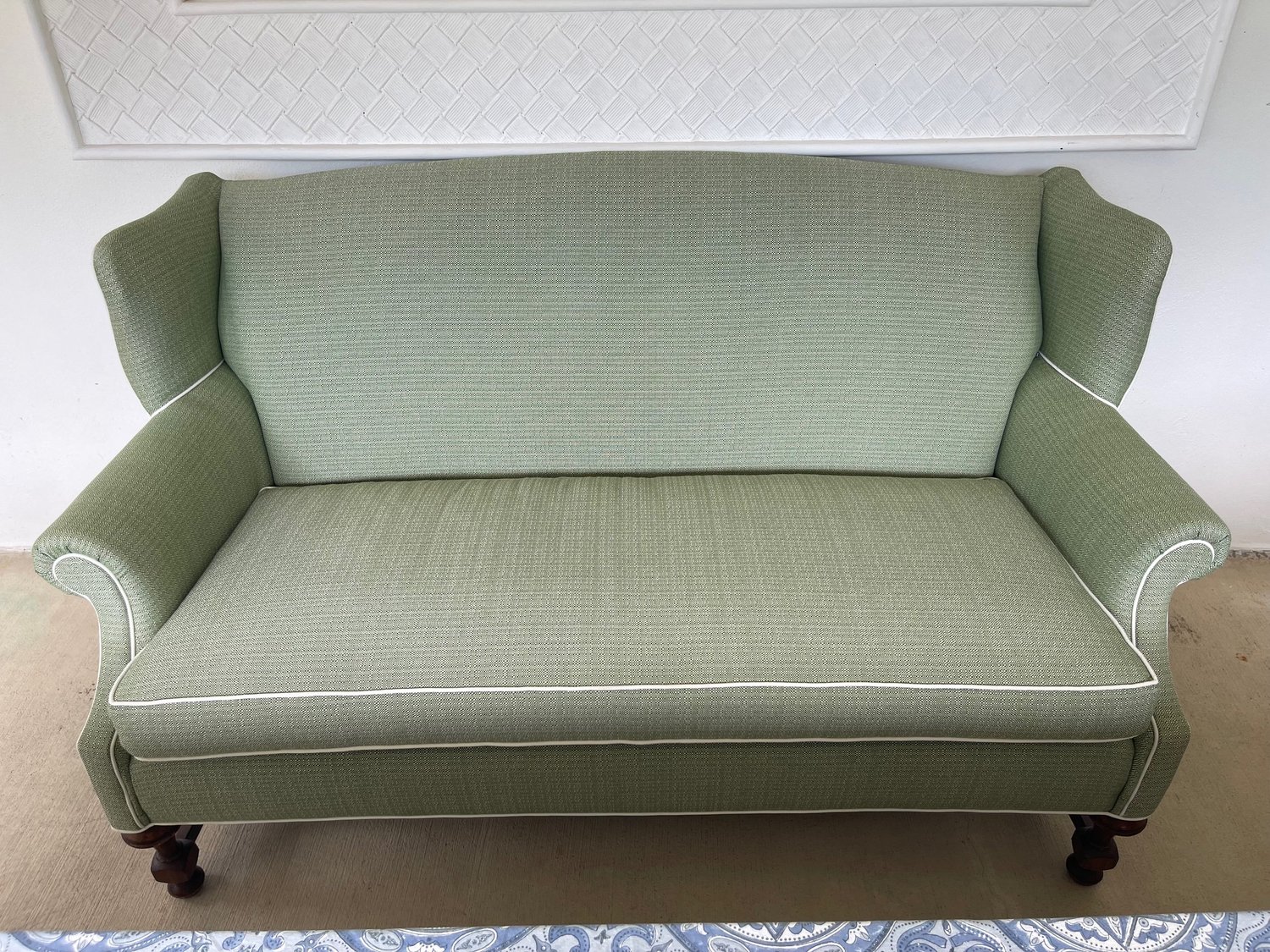A wingback settee with rolled arms in a sage green weave, finished with white piping.