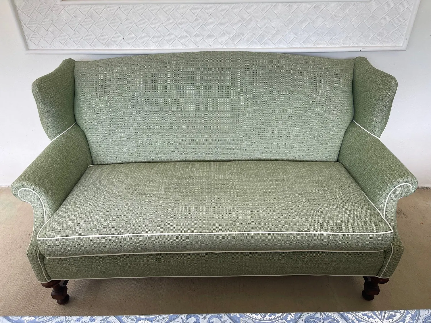 A wingback settee with rolled arms in a sage green weave, finished with white piping.